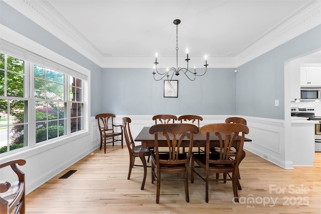 dining space featuring crown molding, visible vents, a chandelier, light wood finished floors, and wainscoting