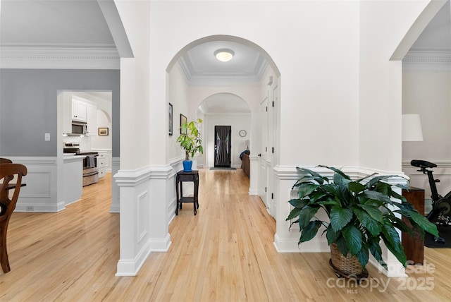 hall featuring ornamental molding, light wood-style flooring, and arched walkways