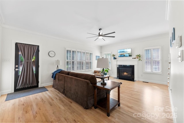 living room featuring crown molding, ceiling fan, a fireplace with flush hearth, and light wood-type flooring