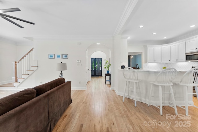 living room featuring crown molding, arched walkways, light wood-type flooring, recessed lighting, and a ceiling fan