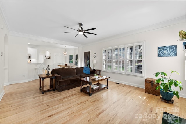 living area with baseboards, arched walkways, ceiling fan with notable chandelier, and ornamental molding