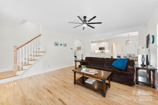 living room with stairway, light wood-type flooring, ornamental molding, and arched walkways