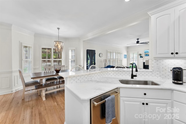 kitchen with a sink, ornamental molding, light wood-style flooring, a peninsula, and stainless steel dishwasher