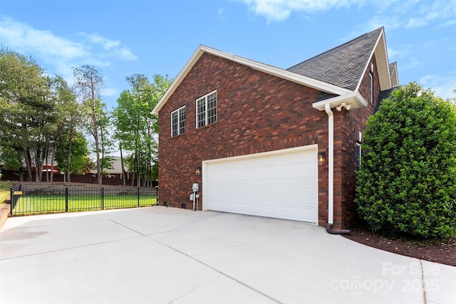 view of side of home with a garage, a shingled roof, driveway, brick siding, and fence