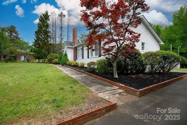 view of side of home with a chimney and a yard