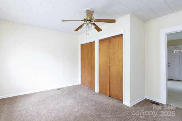 unfurnished bedroom with two closets, a ceiling fan, visible vents, and carpet