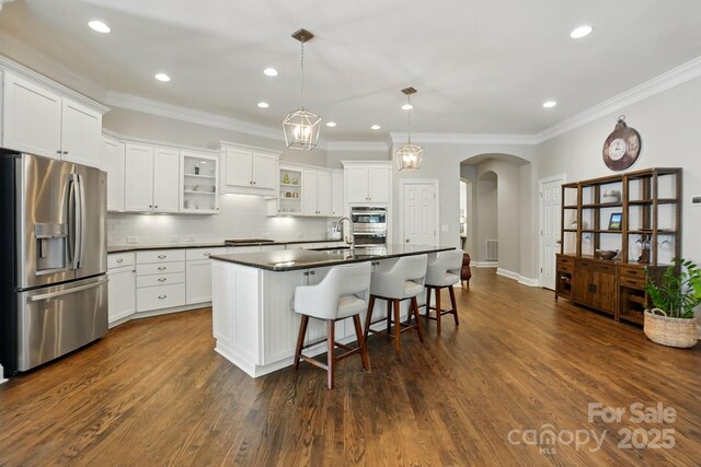 kitchen with crown molding, dark countertops, arched walkways, stainless steel fridge with ice dispenser, and black electric stovetop
