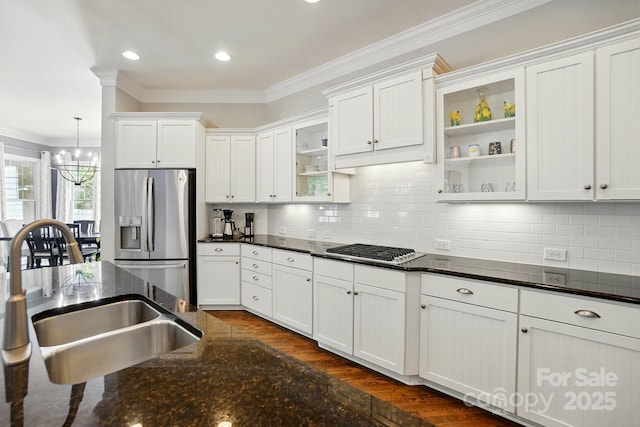 kitchen with crown molding, appliances with stainless steel finishes, a sink, white cabinets, and a notable chandelier