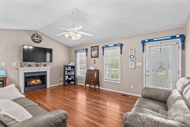 living room featuring light wood-style flooring, plenty of natural light, vaulted ceiling, ceiling fan, and a lit fireplace