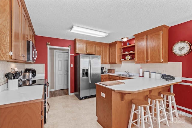 kitchen featuring a sink, brown cabinetry, baseboards, a peninsula, and appliances with stainless steel finishes