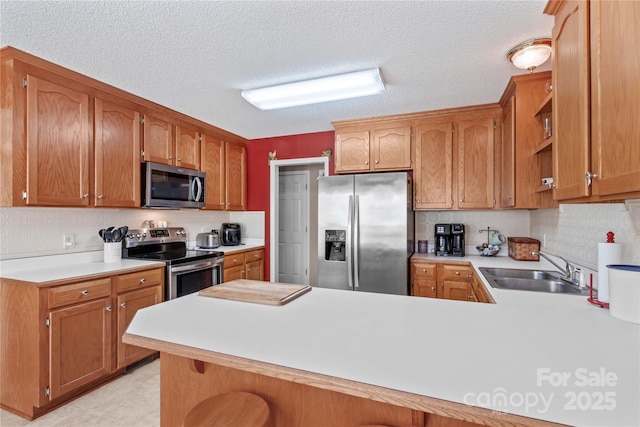 kitchen with a peninsula, light countertops, a sink, and appliances with stainless steel finishes