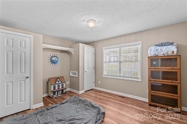 bedroom with wood finished floors, a textured ceiling, baseboards, and visible vents