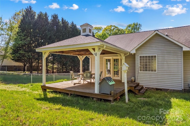 rear view of property featuring fence, a yard, a wooden deck, a gazebo, and roof with shingles