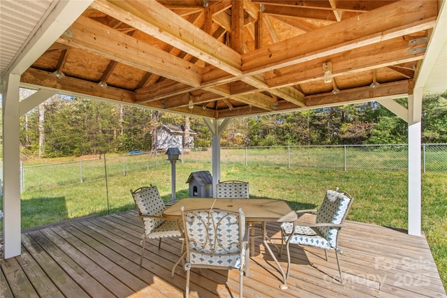 wooden deck featuring a fenced backyard, an outdoor structure, outdoor dining area, a lawn, and a storage unit