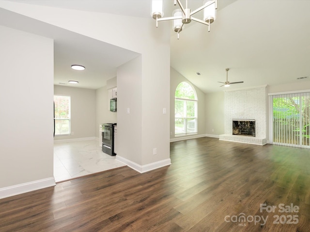 unfurnished living room featuring ceiling fan with notable chandelier, baseboards, wood finished floors, and a brick fireplace