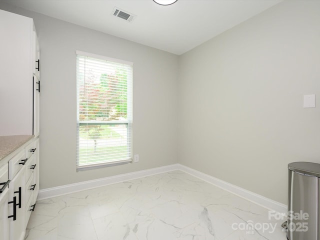 unfurnished dining area featuring marble finish floor, baseboards, a healthy amount of sunlight, and visible vents