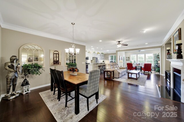 dining space featuring a fireplace, crown molding, dark wood-type flooring, and ceiling fan with notable chandelier