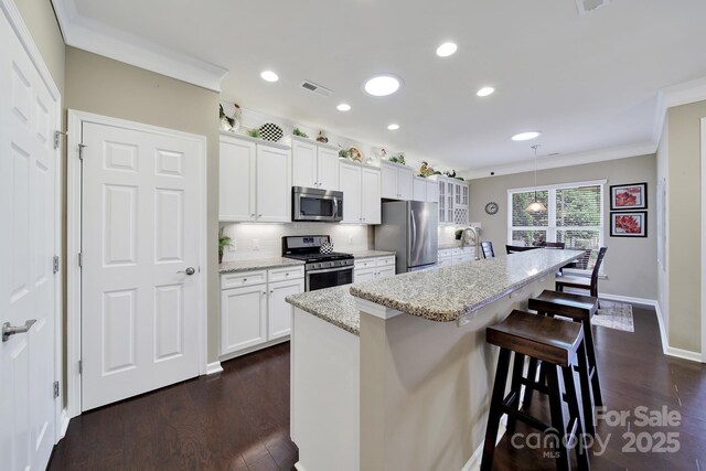 kitchen featuring stainless steel appliances, recessed lighting, a kitchen bar, white cabinetry, and crown molding