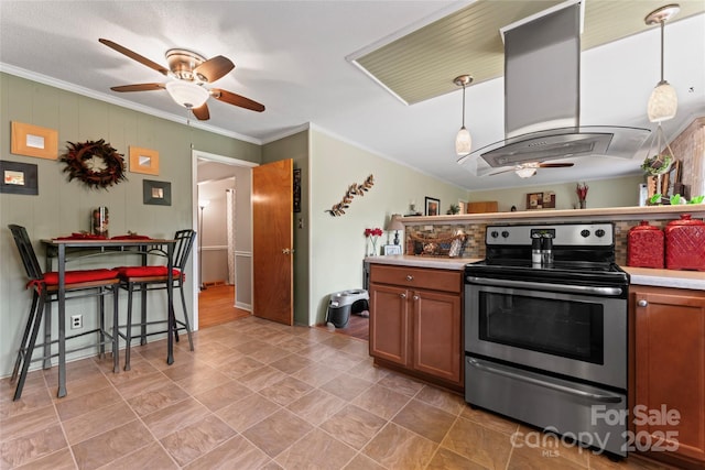 kitchen with island exhaust hood, a ceiling fan, crown molding, brown cabinetry, and stainless steel electric range oven
