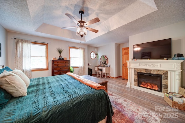 122 Roxboro Ct Unit 286, Mount Gilead, NC 27306 - bedroom featuring light wood-type flooring, a textured ceiling, a glass covered fireplace, and a tray ceiling