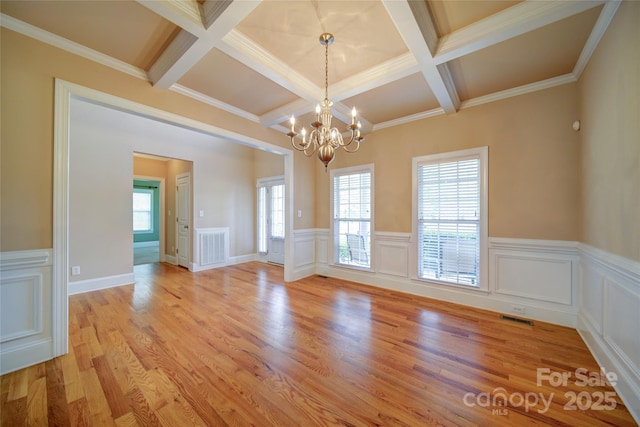 empty room featuring visible vents, a chandelier, coffered ceiling, and a healthy amount of sunlight