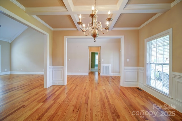 unfurnished dining area featuring light wood-style floors, an inviting chandelier, a wainscoted wall, coffered ceiling, and visible vents