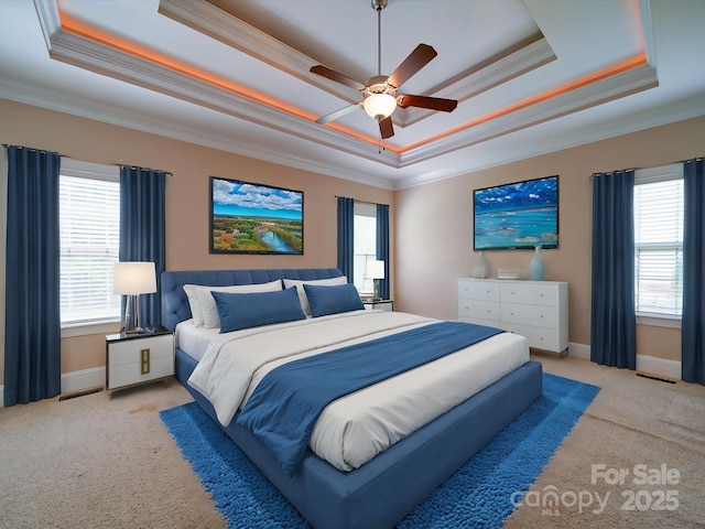 carpeted bedroom with a tray ceiling, ornamental molding, and multiple windows