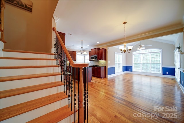 stairway featuring wood finished floors, ceiling fan with notable chandelier, a glass covered fireplace, baseboards, and ornamental molding