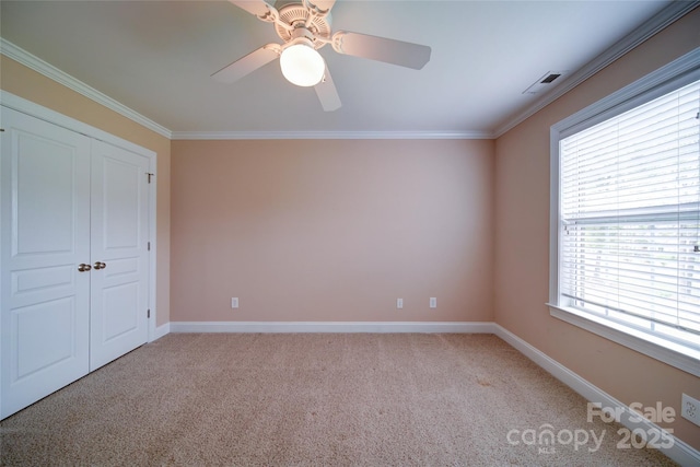 unfurnished bedroom featuring baseboards, visible vents, light colored carpet, and crown molding