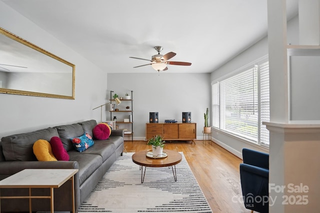 living area featuring light wood finished floors, a ceiling fan, and baseboards