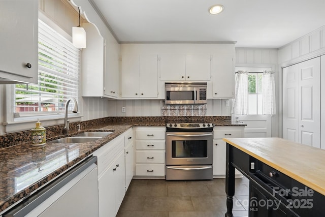 kitchen featuring dark stone countertops, a sink, dark tile patterned flooring, stainless steel appliances, and white cabinetry