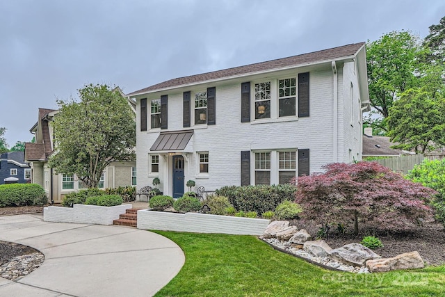 colonial inspired home featuring fence, a front lawn, and brick siding
