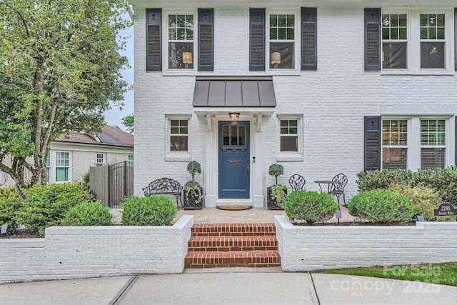 colonial home featuring metal roof, a standing seam roof, fence, and brick siding