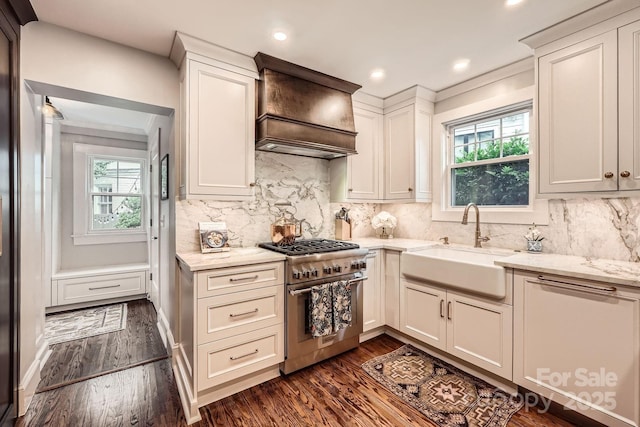 kitchen with light stone countertops, a sink, premium range hood, stainless steel stove, and dark wood finished floors