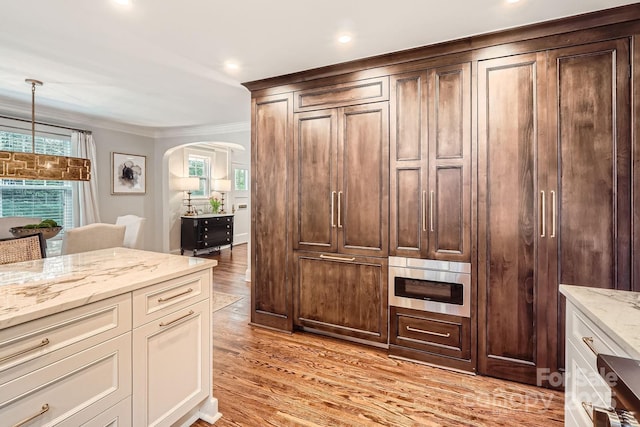 kitchen with light stone counters, arched walkways, light wood finished floors, ornamental molding, and a wealth of natural light