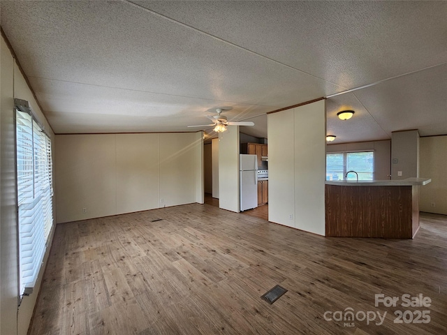 unfurnished living room featuring visible vents, a ceiling fan, a textured ceiling, and wood finished floors