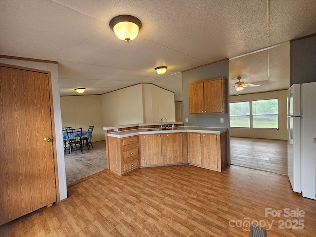 kitchen featuring freestanding refrigerator, a peninsula, light wood-style floors, light countertops, and a sink