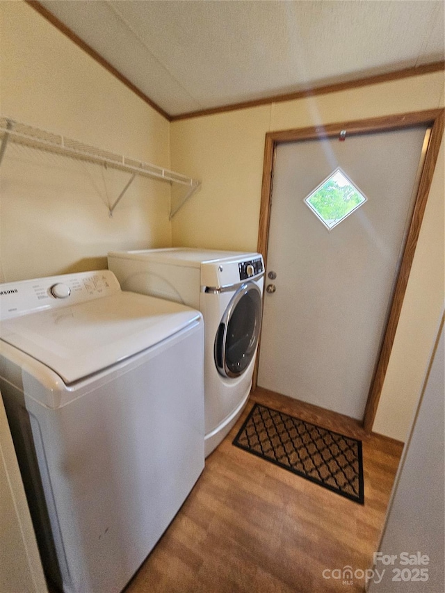 laundry area featuring laundry area, washing machine and dryer, ornamental molding, and light wood-type flooring