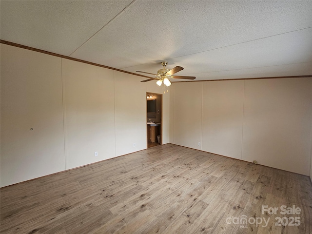 empty room with a ceiling fan, a textured ceiling, crown molding, wood finished floors, and a decorative wall