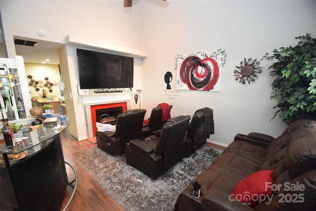living area with a ceiling fan, wood finished floors, visible vents, and a fireplace