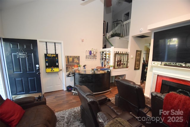 living area with wood finished floors, a towering ceiling, a fireplace, and ceiling fan
