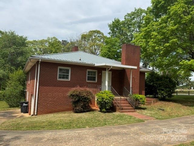 ranch-style home with a front lawn, a chimney, brick siding, and metal roof