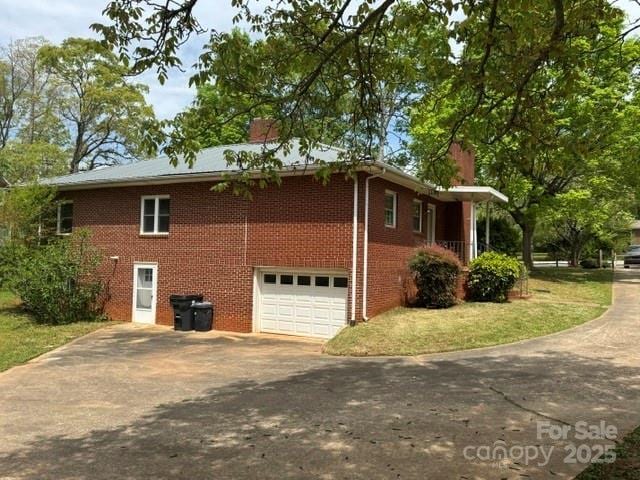view of property exterior with brick siding, an attached garage, and driveway