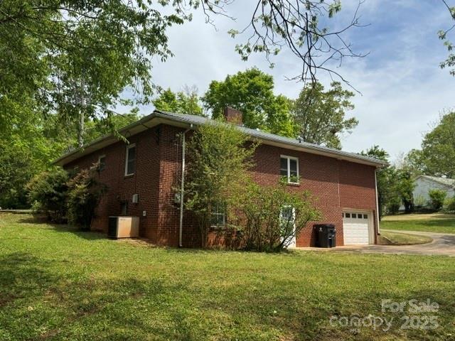 view of home's exterior with a chimney, a lawn, aphalt driveway, a garage, and brick siding