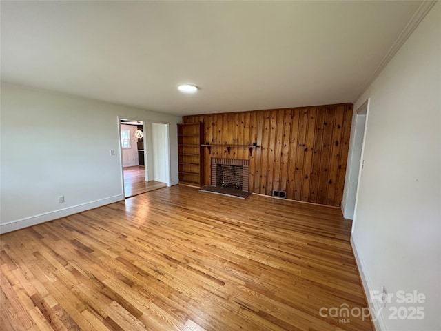 unfurnished living room with light wood-style floors, wooden walls, baseboards, a brick fireplace, and visible vents