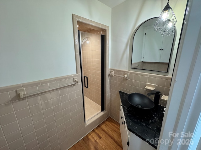 full bath with a shower stall, wood finished floors, vanity, tile walls, and wainscoting