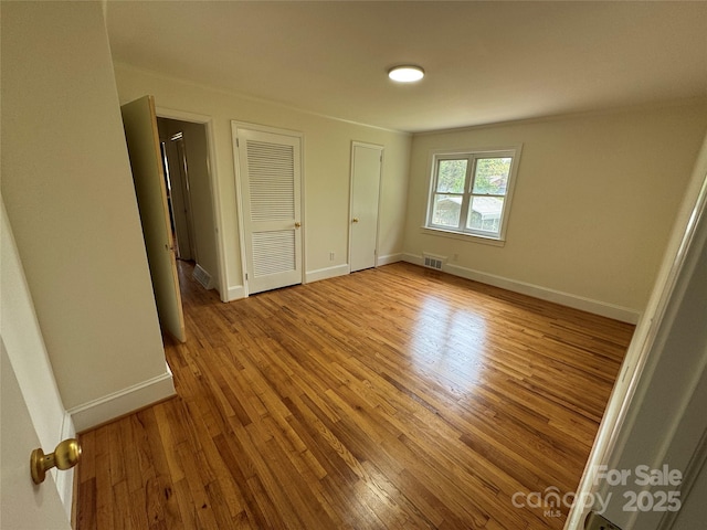 unfurnished bedroom featuring wood finished floors, visible vents, baseboards, and multiple closets