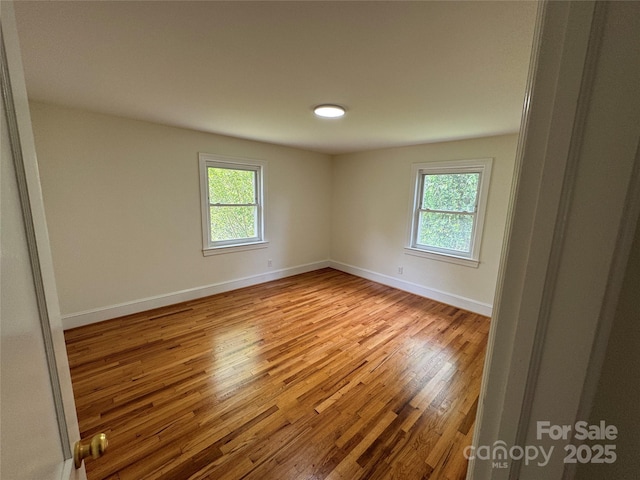 unfurnished room with baseboards, a healthy amount of sunlight, and wood finished floors