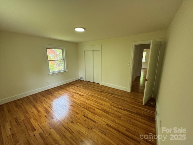 unfurnished bedroom with multiple windows, wood finished floors, and a closet