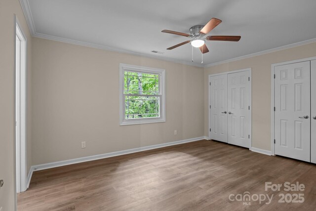 unfurnished bedroom featuring wood finished floors, multiple closets, baseboards, and ornamental molding